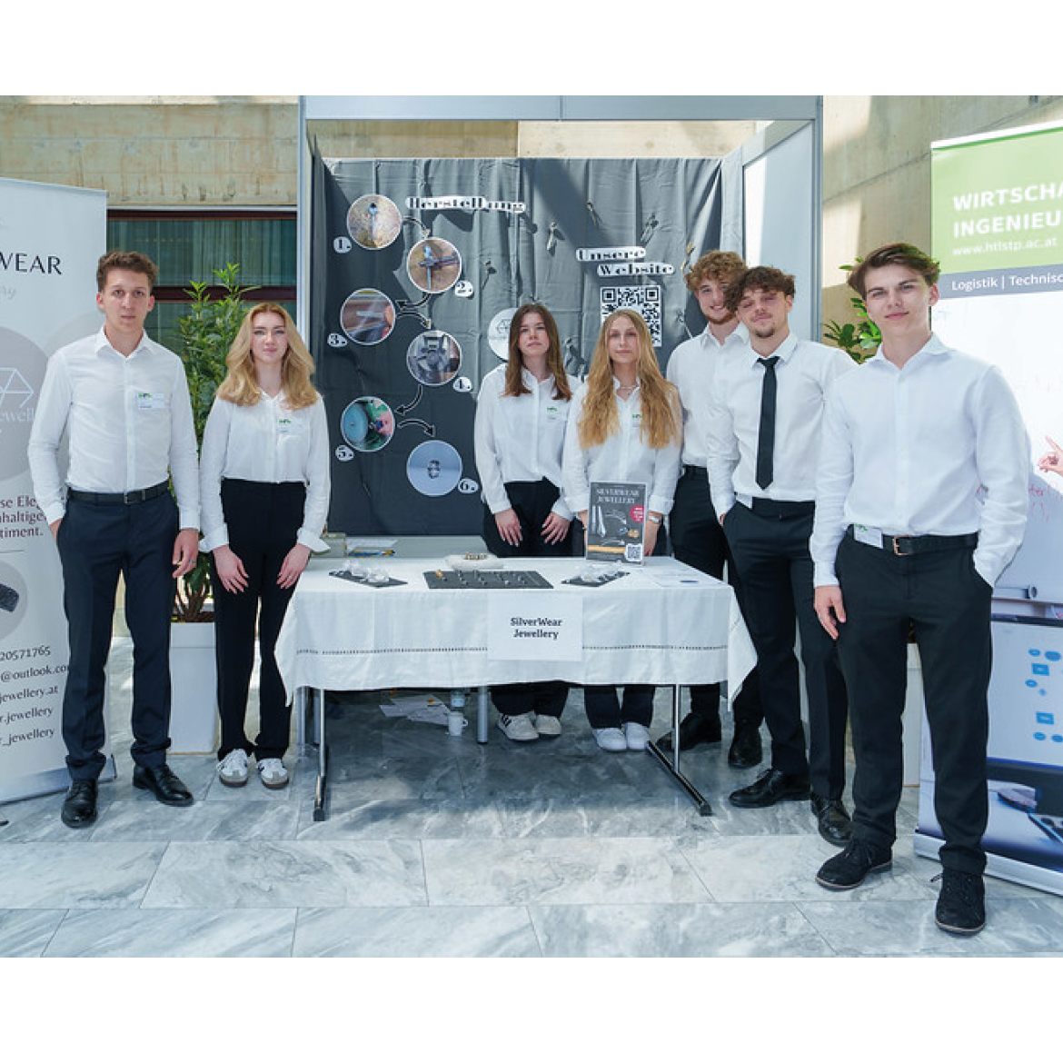 7 Schüler:innen stehen um einen Tisch und präsentieren ihr Angebot auf der Junior Messe NÖ.