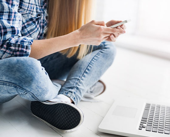 Ein Mädchen mit Handy sitzend vor einen Laptop