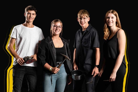 4 junge Menschen stehen vor schwarzem Hintergrund und halten Arbeitsgeräte in den Händen.