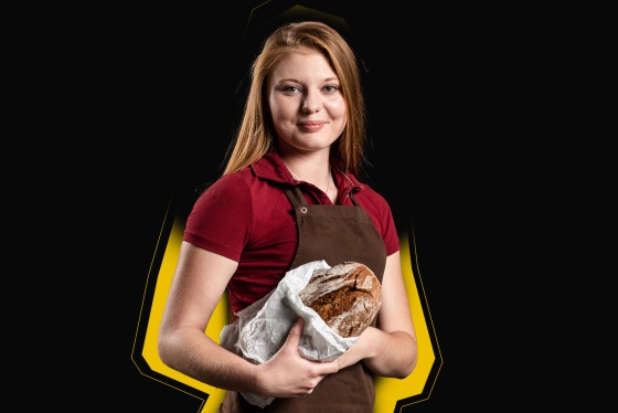 Ein Mädchen in roter Schürze hält einen Laib Brot in der Hand.
