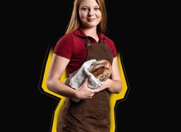 Ein Mädchen mit Schürze und frisch gebackenem Brot in der Hand.